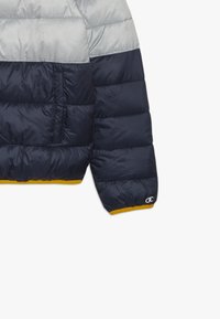 Pufferjacka med färgschema i silver, marinblått och gult. Tillverkad av mjukt, glänsande material med sidoficka och logotypdetalj.