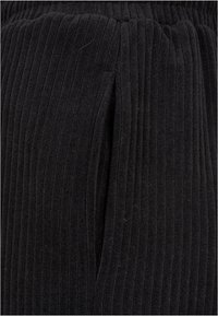 Gros plan d'un tissu noir côtelé avec des lignes texturées verticales et un détail d'ouverture fendue au centre.