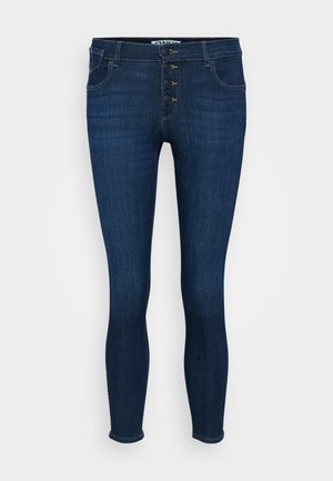 Tumed sinine denim kitsas teksapüksid kõrge taljega, viie tasku ja nööpidega sulgemisega. Sile tekstuur minimaalsete kulumismärkidega.