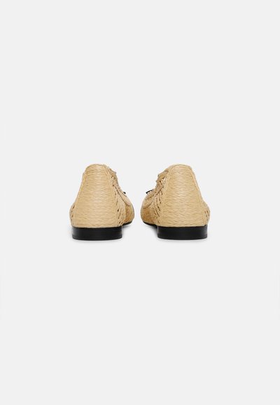 Paire de chaussures beige tissées à enfiler avec des semelles plates noires vues de dos sur un fond blanc uni.