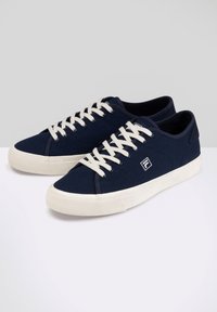 Sneaker in tela navy con lacci bianchi, suole in gomma e dettaglio del logo sul lato. Design classico a basso profilo con punta testurizzata.