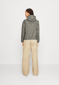 Grey, lightweight, hooded jacket with elastic cuffs and waistband, paired with beige wide-leg pants featuring cargo pockets.
