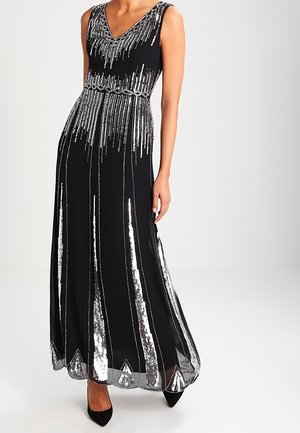 Sleeveless black evening gown with silver sequined vertical stripes and a deep V-neck, worn with black pointed heels.