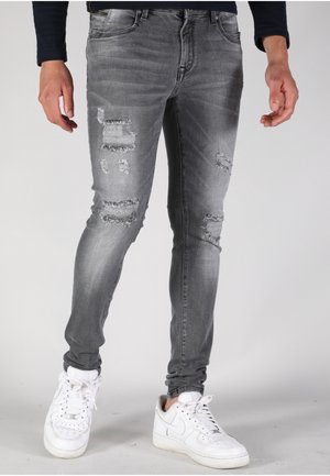 Faded grey skinny jeans with distressed patches, featuring a five-pocket design and a mid-rise waistband, paired with white sneakers.