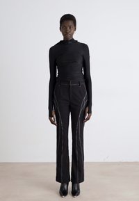Haut noir à manches longues avec col montant, associé à un pantalon noir avec des coutures latérales blanches contrastantes, et des bottines noires.