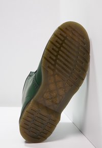 Zielony gumowy but z teksturowaną podeszwą. Charakteryzuje się wypukłym wzorem i przeszywaniem wzdłuż cholewki. Gładkie wykończenie, lekka konstrukcja.