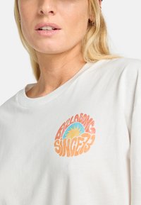 T-shirt di cotone bianco con una grafica circolare con la scritta "Billabong Since 73" in arancione e blu, con un motivo solare al centro.