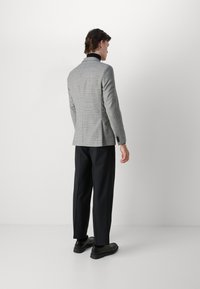 Grå rutig blazer med svart krage, kombinerad med svarta byxor och skor. Blazern har en skräddarsydd passform och en strukturerad design.