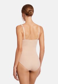 Nude shapewear bodysuit med tunna justerbara remmar, slät textur och åtsittande design som framhäver ryggen och kurvorna.
