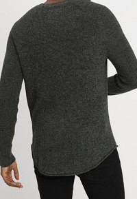 Mörkgrön stickad tröja med rund halsringning, raglanärmar och rundad nederkant. Yttexturen är ribbad och mjuk.