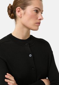 Zwarte gebreide cardigan met een ronde hals, voorzien van twee knopen, een gladde textuur en een aansluitend ontwerp dat het lichaam volgt.