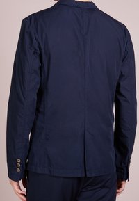 Granatowa, lekka kurtka wykonana z tkaniny o gładkiej fakturze. Posiada wentylację z tyłu oraz mankiety zapinane na guziki dla dodatkowych detali.