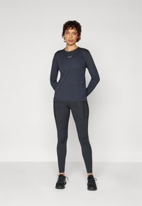 Langarm-Navy-Sportoberteil kombiniert mit schwarzen Leggings, mit slim Fit, weichem Material und minimalistischer Gestaltung mit Logodetails.