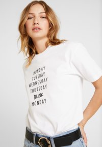 Witte katoenen t-shirt met korte mouwen met zwarte tekst: "MAANDAG DINSDAG WOENSDAG DONDERDAG KNIPPER MAANDAG." Casual pasvorm.