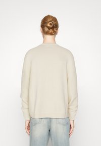 Pull en maille couleur crème avec une coupe décontractée, des poignets et un ourlet côtelés. Design simple, sans motifs ni détails en métal visibles.