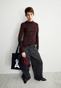 Langarm-Oberteil mit zebra-marmorn Streifen in Dunkelrot, hochtaillierte graue weit geschnittene Jeans, marineblaue Tasche mit weißem Logo, dunkelrote Kappe, schwarze spitze Schuhe.