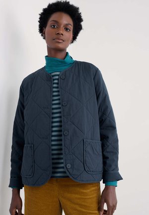 Gewatteerd marineblauw jack met ronde hals, knoopsluiting aan de voorkant en twee zakken aan de voorkant. Daaronder een groen-blauw gestreepte coltrui.