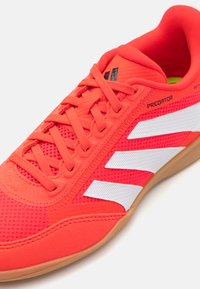 Rød sportsko med mesh- og syntetisk overdel, som har hvite tre striper, teksturerte detaljer og en gummirikgummi-såle. Snøringsdesign.