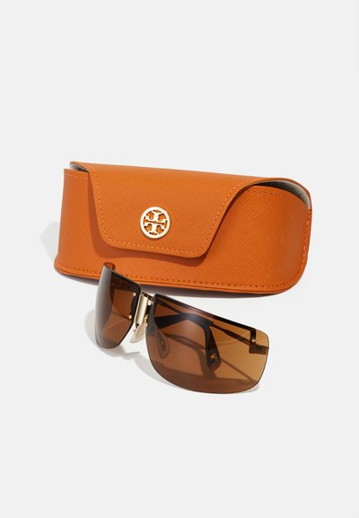 Lunettes de soleil avec des verres marron et une forme géométrique épurée, placées à côté d'un étui texturé orange avec un accent logo doré.
