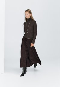 Brown turtleneck sweater, black suede maxi skirt, and black heeled boots. Long hair, simple silver pendant necklace, minimalist background.