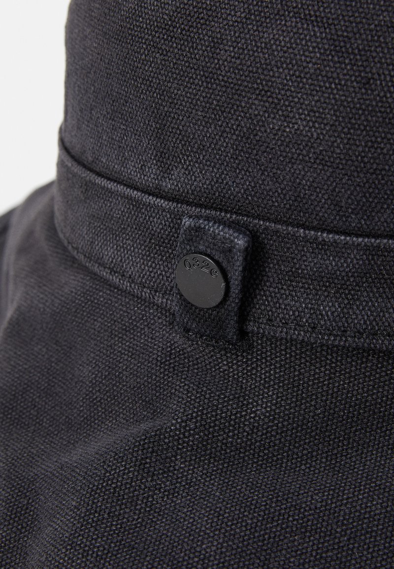 Black fabric hat with a textured finish, featuring a rounded crown, short brim, and a black snap button accent.
