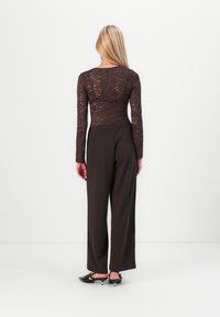 Brun blonde langermet topp med en tettsittende kropp, kombinert med vide brun bukser og svarte snikers med spisser og sløyfer.