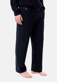 Marinblå joggebukser med teksturert finish, med grønne sidestriper og elastisk liv. Lacoste-logo på venstre overbein.