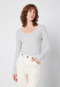 Camisola de manga longa em cinza claro com decote em V, feita de um tecido suave; combinada com calças em marfim com botões castanho-escuro e bolsos laterais.
