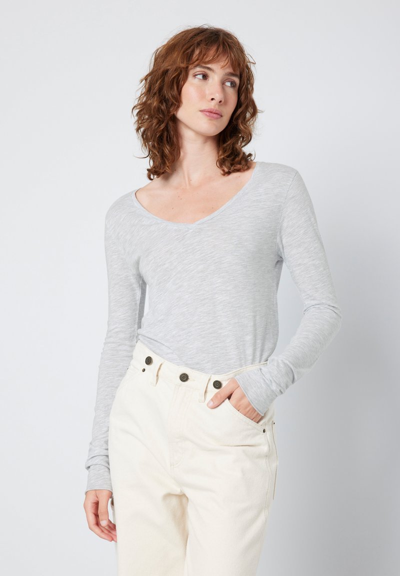 Camisola de manga longa em cinza claro com decote em V, feita de um tecido suave; combinada com calças em marfim com botões castanho-escuro e bolsos laterais.