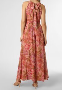 Květinové maxi šaty v růžových odstínech, mají šněrování na zádech, splývavý střih a vzor velkých pivoňek se zelenými listy. Hladká struktura materiálu.