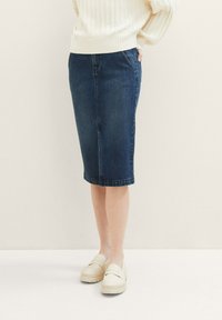 Falda lápiz vaquera en azul oscuro, con un diseño ajustado, corte hasta la rodilla y detalles de costuras tonales. Combinada con mocasines de color crema.