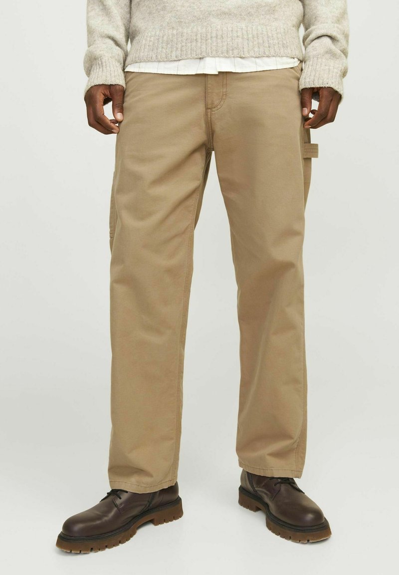 Beige cargobroek met zijzakken, gemaakt van stevig materiaal. Rechte pijpen met zichtbare stiksels, gecombineerd met bruin veterlaarzen.