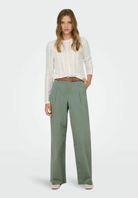 Lightweight, cream knit top with long sleeves and textured design, paired with high-waisted, wide-leg olive green pants and brown belt.