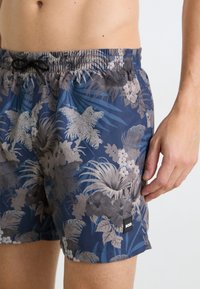 Șorturi de înot de marină, cu un model floral tropical în nuanțe de gri, având o talie elastică și un mic logo cusut în partea de jos.