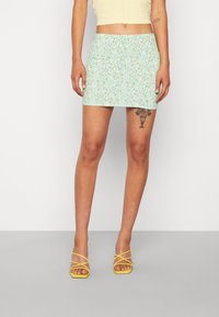 Saias mini florais em azul claro com um design justo, apresentando pequenos padrões de flores multicoloridas. Combinada com sapatos de salto alto amarelados com tiras.