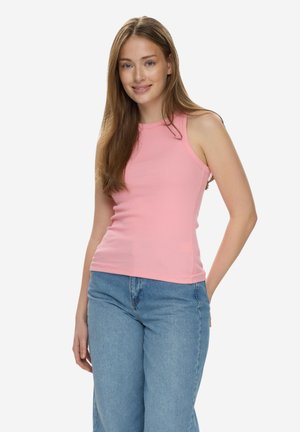 Joven con cabello largo, vistiendo una camiseta sin mangas rosa y jeans azules, sonriendo y posando con una mano detrás de la espalda.