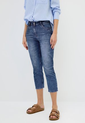 Jeans capri in denim azzurro chiaro con una finitura leggermente usurata, tasche anteriori e un design aderente. Abbinati con sandali marroni.