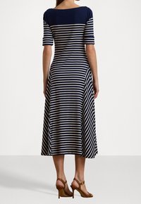 Úzké pruhované šaty v námořnické modři a krémové barvě s těsným korzetem a rozevlátou sukní, krátkými rukávy a kulatým výstřihem. Nosené s hnědými sandály na podpatku.