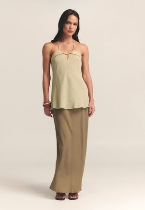 Lys grøn ærmeløs top med en nøglehul detalje, parret med en lang brun nederdel. Glat tekstur med en subtil glans, flade sandaler.