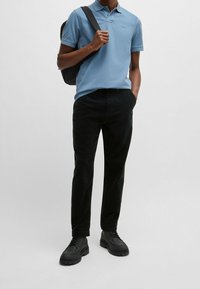 Jasnoniebieska koszulka polo z kołnierzykiem, zestawiona z czarnymi spodniami sztruksowymi i czarnymi sznurowanymi butami. Torba przewieszona przez jedno ramię.