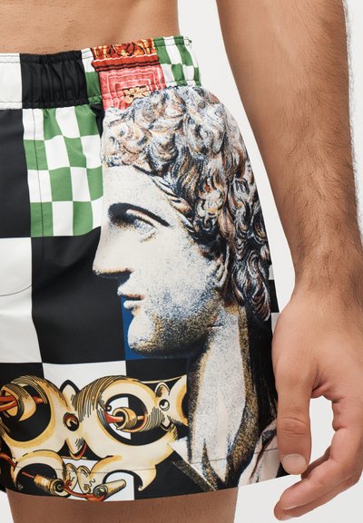 Κλείσιμο εικόνας ενός ατόμου που φοράει σορτς με λεπτομερή κλασικό γλυπτό κεφαλής, πράσινο και μαύρο σκακιέρα και περίτεχνα κίτρινα σχέδια.