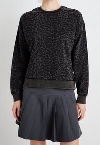 Sweatshirt noir avec motif léopard, col et poignets côtelés, associé à une jupe plissée gris foncé. Texture douce, design décontracté.
