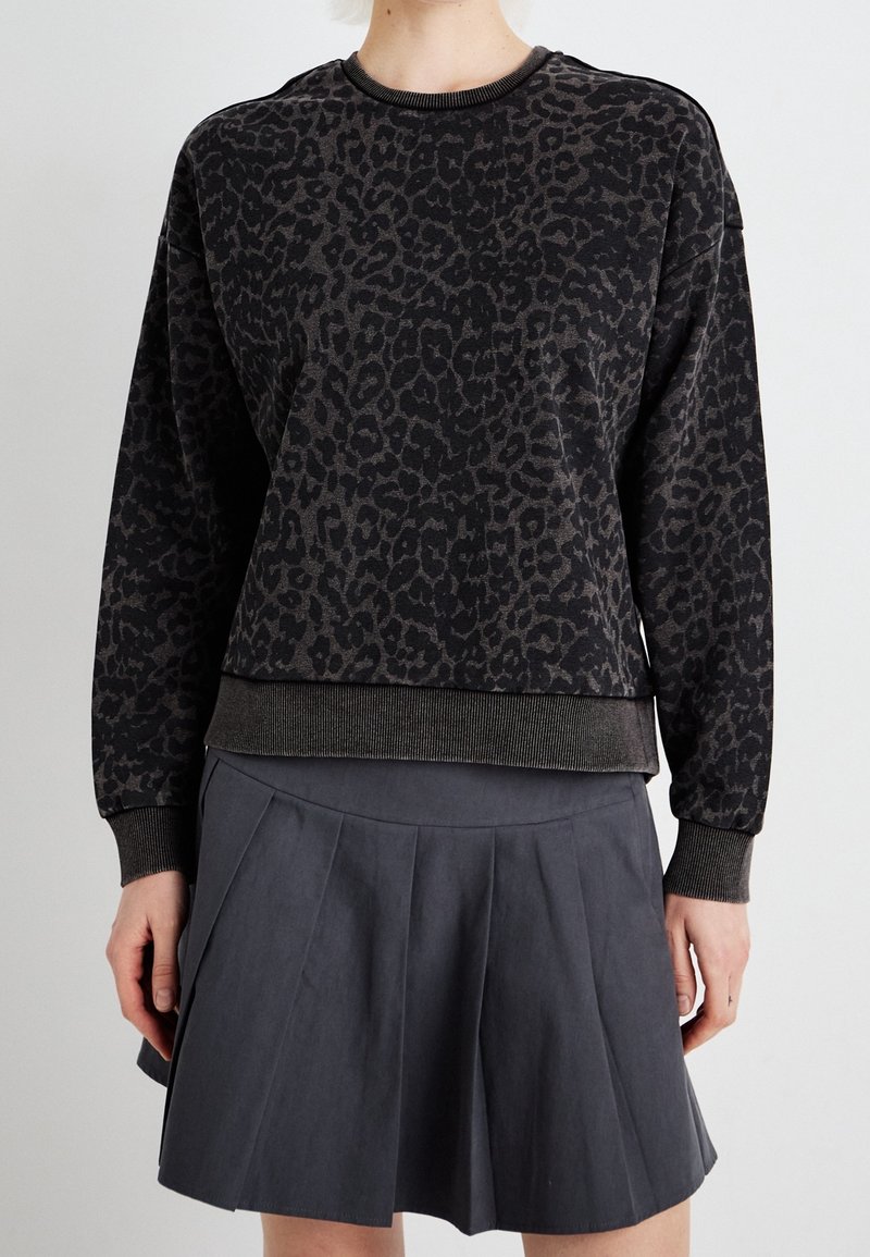 Sweatshirt noir avec motif léopard, col et poignets côtelés, associé à une jupe plissée gris foncé. Texture douce, design décontracté.