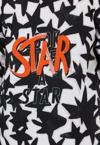 Zwart-witte lange mouwen shirt met stervormen en de tekst "KIJK EEN STER" in vette oranje en zwarte letters. Katoenen materiaal.