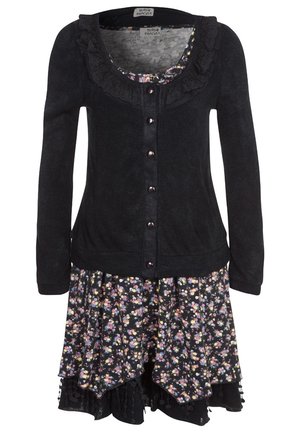 Cardigan noir à manches longues avec un col à volants, porté sur une robe à volants à motifs floraux multicolores.