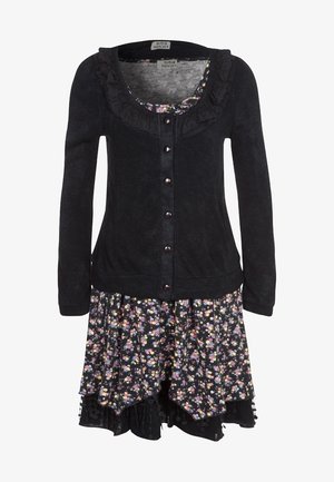 Černý dlouhý cardigan s volánkovým výstřihem přes vrstvené květinové šaty s malými víceméněbarevnými květy.