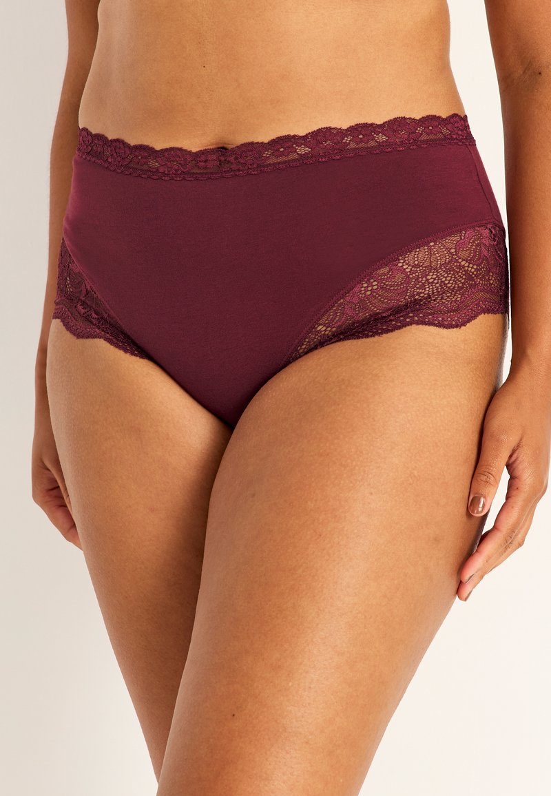 Mörkröda högmidjade underkläder med blommönstrad spetsdetalj längs midjan och sidan. Lyxig struktur med vågiga spetskanter.