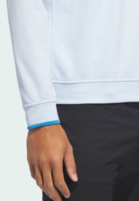 Jasnoniebieska bluzka z długim rękawem o teksturowanym wzorze, z kontrastowymi, niebieskimi wykończeniami na mankietach, zestawiona z czarnymi spodniami.