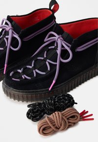 Μαύρα σουέτ παπούτσια με παχύ διαφανές πάτο, διαθέτουν πολύχρωμους πλεχτούς κορδόνες και δύο επιπλέον επιλογές κορδονιών σε μαύρα και πορτοκαλί σχέδια.