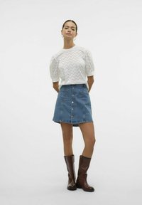 Hvid kortærmet top med tekstureret mønster; blå denim A-linje nederdel med knapper; brune læderstøvler til knæene.